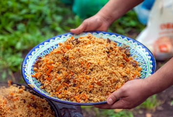 Men's hands hold a colored plate with Uzbek pilaf close-up in summer