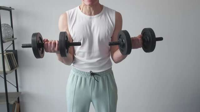Hard sport. Exhausted man. Home powerlifting. Unrecognizable casual guy suffering doing workout with dumbbells in light room interior.