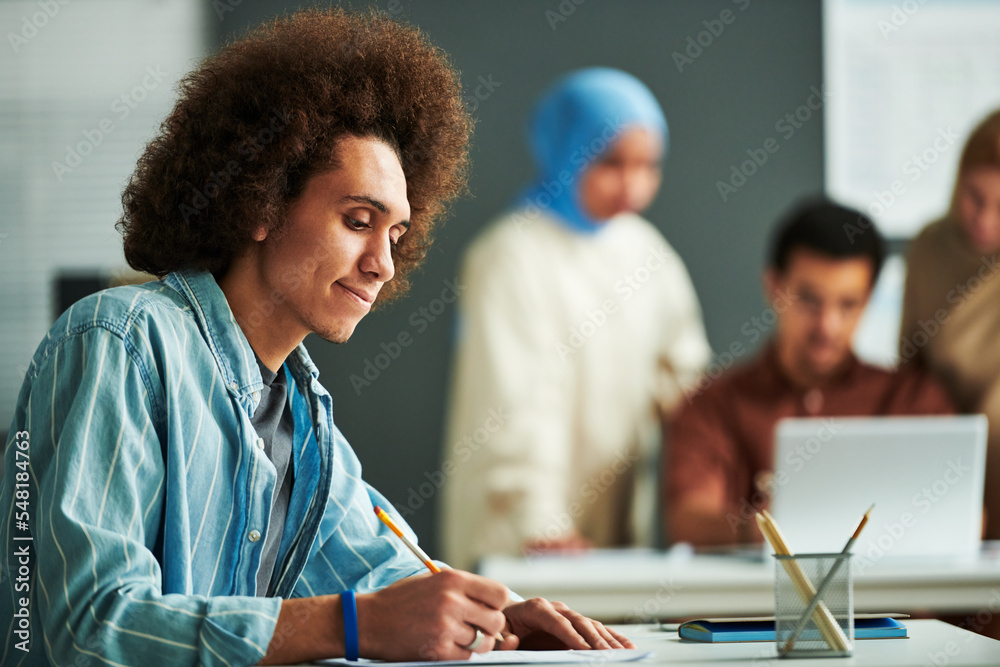Poster Side view of young multi-ethnic student looking at paper with grammar test and pointing at it while thinking of right answer at lesson
