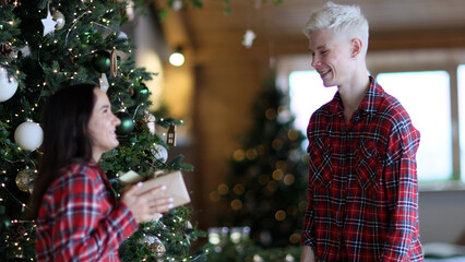 Young blond man gives gift box for a woman smiling and thanking handsome husband standing with her