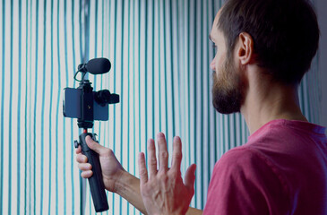 A young blogger records a video with himself on his smartphone in his room studio