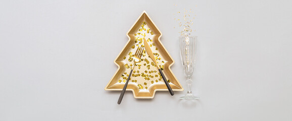 Plate in shape of Christmas tree with confetti, cutlery and champagne glass on light background