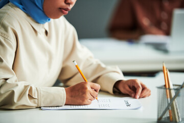 Hand of young Muslim female student with pencil over paper with grammar test ticking right answers during individual work - obrazy, fototapety, plakaty