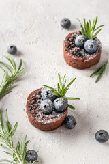 Two chocolate brownies decorated with blueberries and sugar powder on white textured background. Christmas, New Year recipe concept