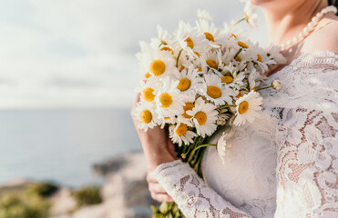 summer bouquet of field daisies in the hands of a bride in white