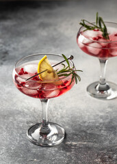 Two wineglass of Pomegranate Christmas cocktail with rosemary and lemon on gray background isolated with text space. Xmas drink