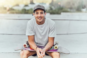 Fotobehang Skateboard Young man, skateboard and skater with music at urban skate park, youth and recreation with earphones for audio streaming. Happy, portrait, and gen z outdoor with skating practice and fitness.  © Clement C/peopleimages.com