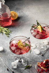 Two wineglass of Pomegranate Christmas cocktail with rosemary and lemon on gray background with text space. Xmas drink