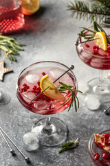 Two wineglass of Pomegranate Christmas cocktail with rosemary and lemon on gray background with fir branches close up. Xmas drink