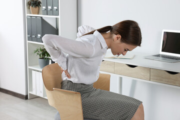 Woman suffering from back pain while sitting in office. Symptom of scoliosis - obrazy, fototapety, plakaty