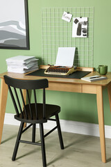 Typewriter, stack of papers and mood board on wooden table near pale green wall. Writer's workplace
