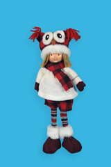 Christmas doll dressed in a checkered scarf, shorts and hat imitating an owl, isolated on a blue background. Festive handmade decorations.