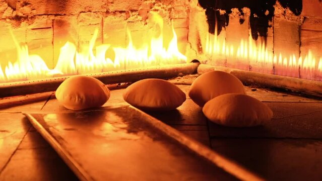 Slow-motion view of a metallic pan moving pita bread pieces baking in a fire oven