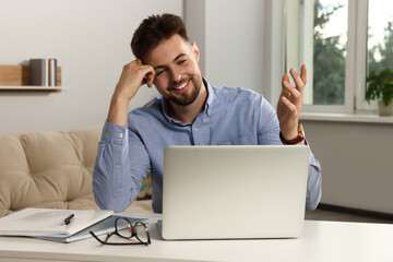 Handsome man working with laptop at table indoors