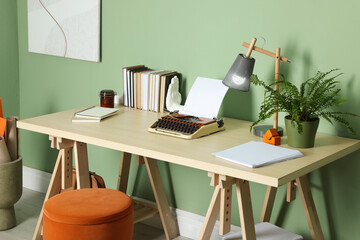 Writer's workplace with typewriter on wooden desk near pale green wall in room