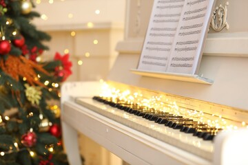 White piano with festive decor and note sheets indoors. Christmas music