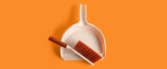 Dustpan and brush on orange background, top view