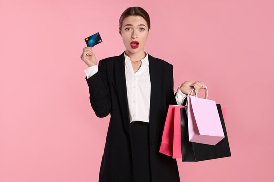 Surprised young woman with shopping bags and credit card on light pink background. Big sale