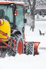 Tractor cleaning urban park paths on a cold snowy day.