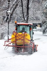 Tractor cleaning urban park paths on a cold snowy day.