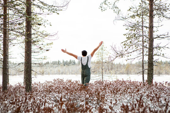 An athletic man raising his hands up with clean snow in the woods. Brutal man hardens to increase immunity. Nature power antistress winter concept