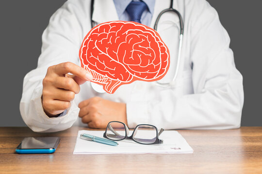 Doctor in a uniform holding a brain symbol made from red paper while sitting at the table