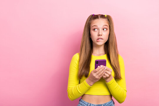 Photo of worried nervous lady wear stylish clothes look empty space bite lips failure spoiled new gadget isolated on pink color background