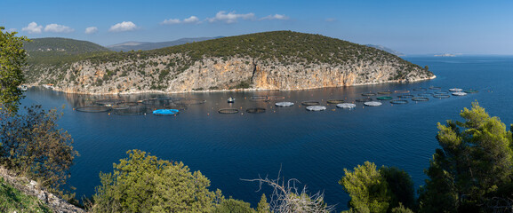 panorama view of a small ocean cove on the coast of the Peloponnese in Greece with aquaculture fish culture nets and maintenance boat
