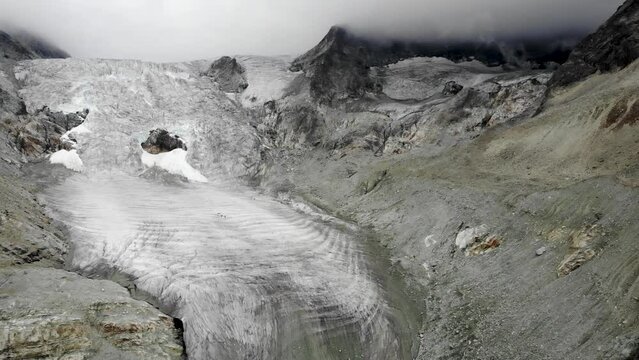 Fast aerial flyover away from the Moiry glacier near Grimentz in Valais, Switzerland with a panoramic view of the ice and crevasses on an overcast summer day