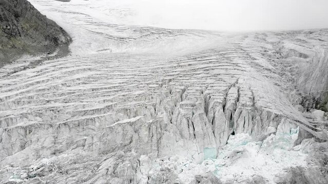 Aerial flyover above the Moiry glacier near Grimentz in Valais, Switzerland with a pan down view of the icy crevasses on an overcast summer day