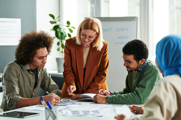 Successful teacher consulting one of young students at lesson while pointing at his notes during...