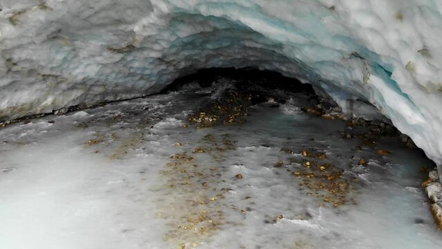 Aerial flyover away from the ice cave of the Zinal glacier in Valais, Switzerland with a pan up view from the melting glacial water stream up to the alpine valley
