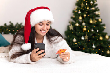 Merry Christmas. A beautiful young woman makes purchases on her smartphone via the Internet. Pay for online shopping. Lifestyle.