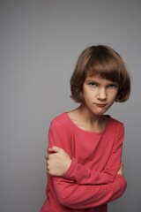 The little girl is angry, taking great offended. The hands are crossed. Gray isolated background.