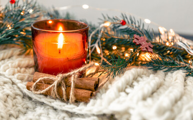 Christmas composition with candle and cinnamon sticks on blurred background.