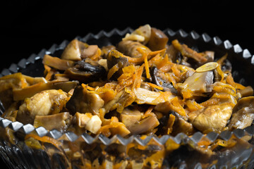 Close-up of pickled mushrooms with carrots in a glass bowl on a black background. Snack, food