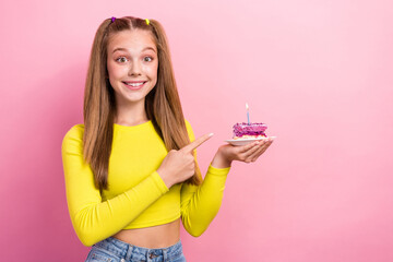 Photo of excited sweet schoolgirl wear yellow crop top pointing cake piece plate empty space isolated pink color background