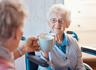 Senior woman, happy friends and toast coffee in wheelchair in room, house or nursing home together....