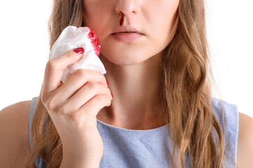 Young woman with nosebleed and tissue on white background, closeup