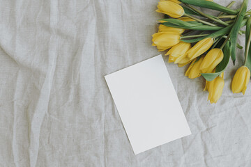 Blank paper invitation card with copy space. Yellow tulip flowers bouquet on neutral linen cloth...