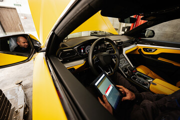 Mechanic using digital tablet, while sitting in yellow sport car suv.