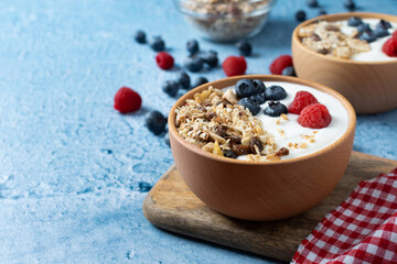 Yogurt with berries and muesli for breakfast in bowl on blue background. Copy spacxe