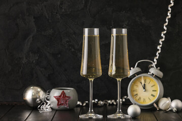 Glasses of champagne, Christmas decorations and alarm clock on table against dark background