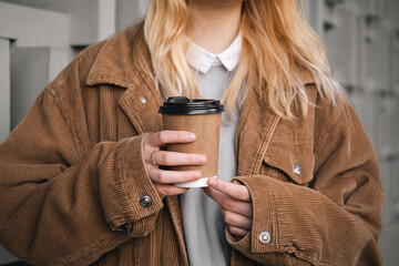 A glass of coffee in the hands of a woman in a corduroy jacket, close-up. - obrazy, fototapety, plakaty