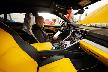 Mechanic using digital tablet, while sitting in yellow sport car suv.