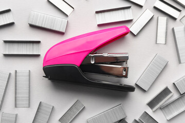 Pink office stapler with staples on light background, closeup
