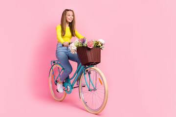 Full length photo of sweet excited school girl dressed yellow crop top driving bicycle looking empty space isolated pink color background