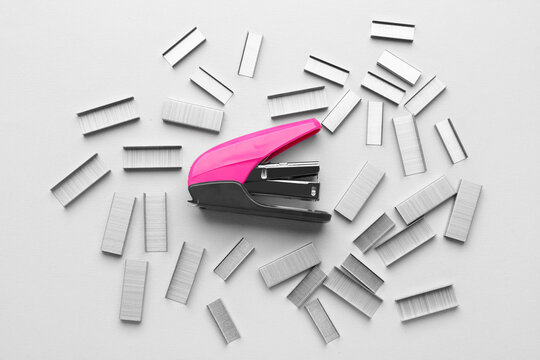 Pink office stapler with staples on light background