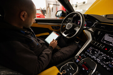 Mechanic using digital tablet, while sitting in yellow sport car suv.