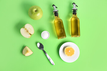 Composition with bottles of apple cider vinegar, fruits and salt on green background
